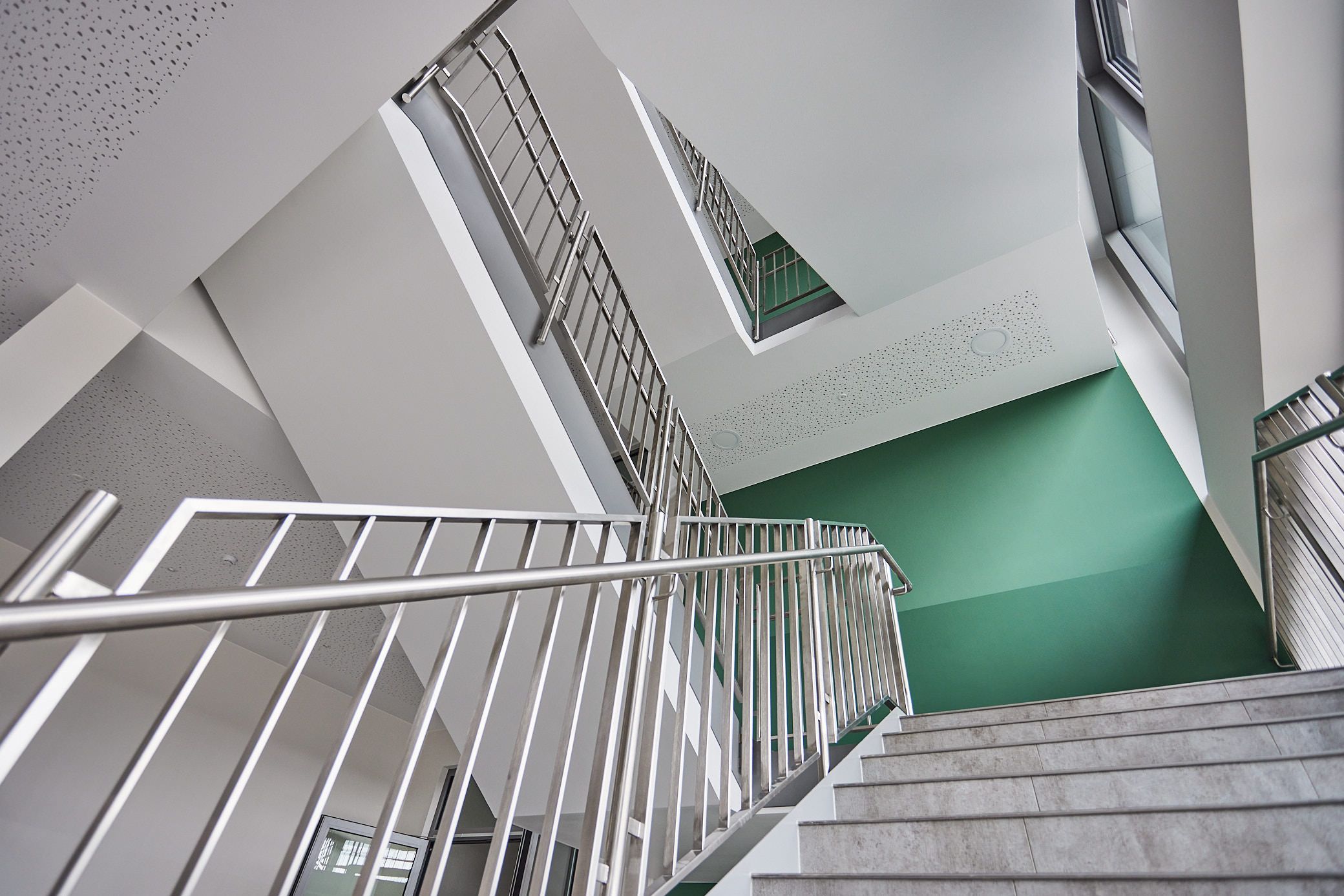 Treppenhaus der Gesamtschule Detmold. Grüne Wand. Metallhandlauf. Ein Projekt von EPU ARCHITEKTEN.
