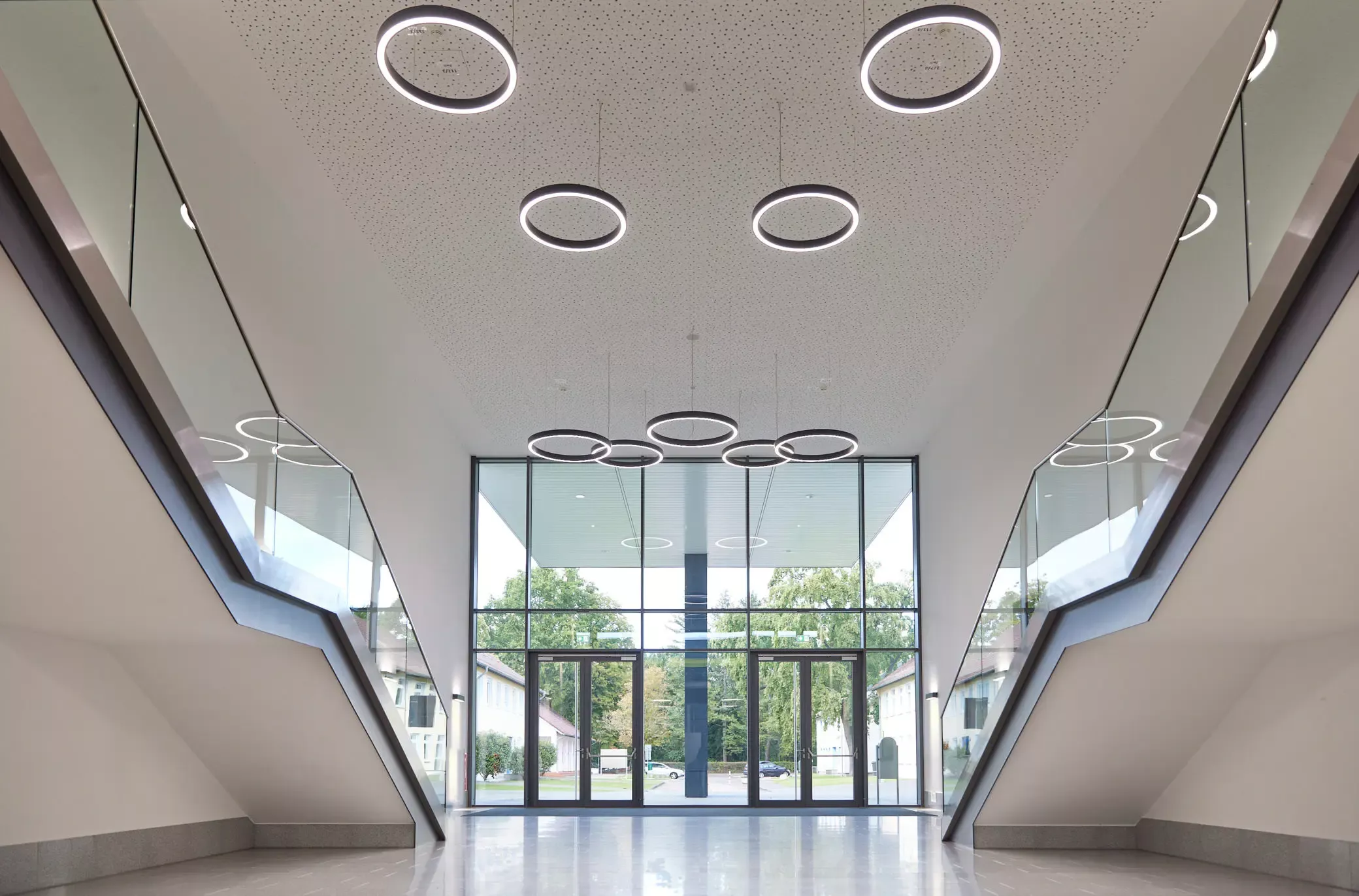 Verglaster Eingang im Foyer. Treppe mit Wandbeleuchtung. Hohe Decke mit runden Leuchten. Ein Projekt von EPU ARCHITEKTEN.